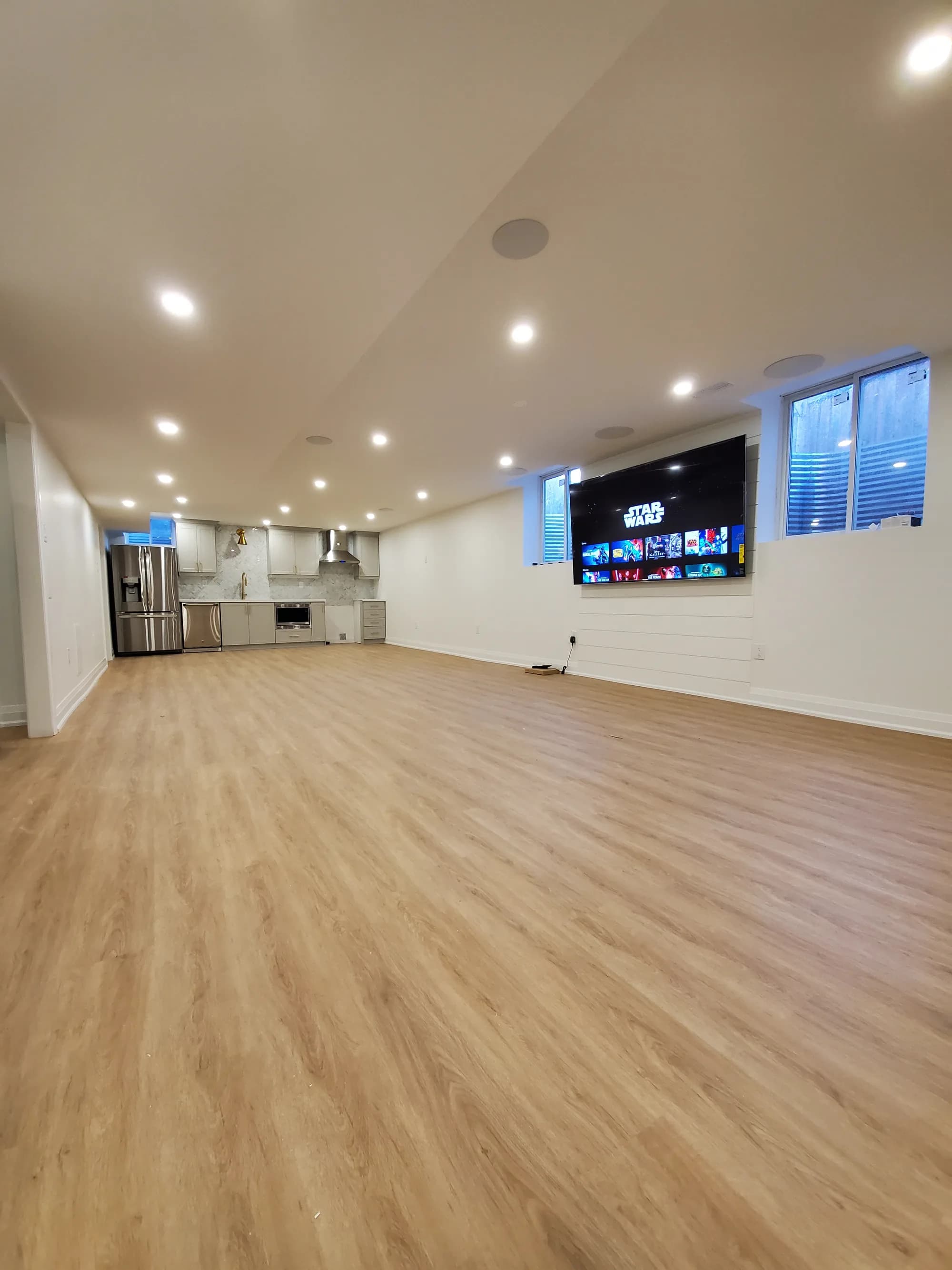 Open finished basement with white shiplap wall, full kitchen, and entertainment area